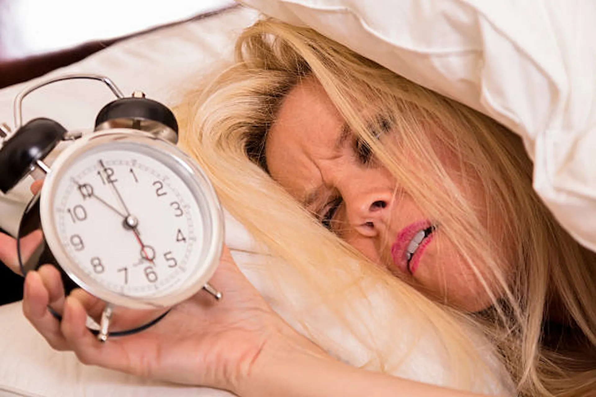 Mujer con insomnio no se puede dormir y mira el despertador con desesperación